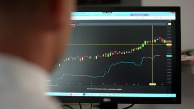Person betrachtet Kurschart mit Kerzen am Monitor im Büro