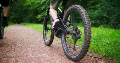 Nahaufnahme eines Mountainbikes mit tretenden Beinen auf dem Waldweg
