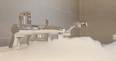 Glänzende Chromarmatur einer Badewanne über aufsteigendem Schaum