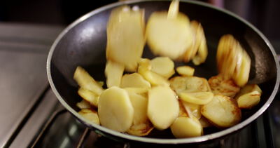 Goldene Kartoffelscheiben werden in der Pfanne geschwenkt und knusprig gebraten