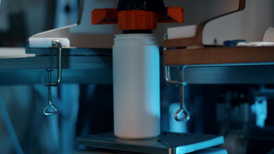 Weiße Plastikflasche an einer Abfüllmaschine im blauen Licht