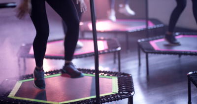 Reihe von Trampolinen springt synchron unter violettem Studiolicht