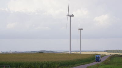 Windräder in Feldlandschaft mit Lastwagen auf Landstraße, Windkraftanlage, Windpark und Ackerland als 4K Stockvideo