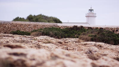 Weißer Leuchtturm hinter einer Trockenmauer an der Felsküste