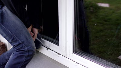 Einbrecher hebelt mit einem Werkzeug ein Fenster auf