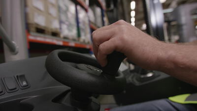 Staplerfahrer greift das Lenkrad eines Gabelstaplers im Lager Staplerfahrer greift das Lenkrad eines Gabelstaplers im Lager, Drehknauf, Gabelstapler fahren und Lagerarbeiter als 4K