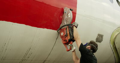 Mann trennt einen Flugzeugrumpf mit einem Trennschleifer nahe dem roten Zierstreifen