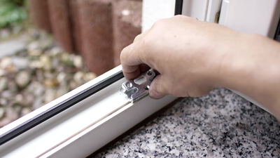 Monteur setzt einen Metallbeschlag von Hand in den Fensterrahmen ein