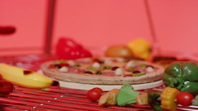 Pizza und Paprika auf einem runden Grillrost vor rotem Hintergrund