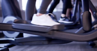 Weiße Sportschuhe drücken Pedale eines Crosstrainers im Fitnessstudio