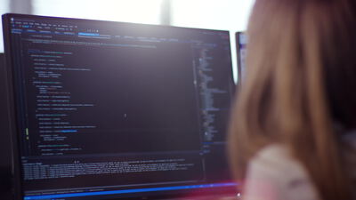 Blick über die Schulter auf Programmcode an einem Monitor