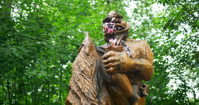 Geschnitzte Holzfigur mit Maske im sommerlichen Wald