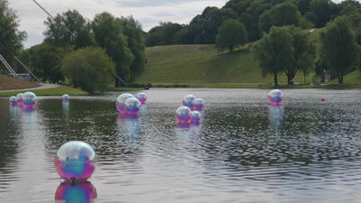 Schillernde Wasserbälle treiben auf einem weiten Parksee: Wasserbälle auf dem See, schillernde Kugeln