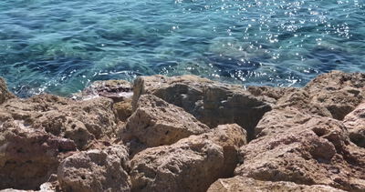Klares türkises Wasser umspült raue Uferfelsen in Nahaufnahme