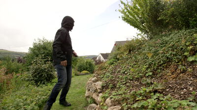 Person in Kapuzenjacke geht durch einen Hanggarten am Dorfrand