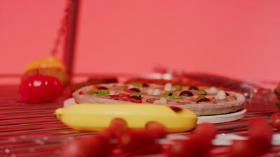 Pizza auf einem Drahtregal mit buntem Obst und Gemüse vor rotem Hintergrund