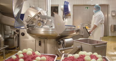 Mitarbeiter bedient den Kutter mit Hackfleisch und Zwiebeln