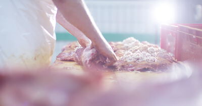 Metzger greift gewürzte Fleischstücke auf einem Holztisch im hellen Gegenlicht
