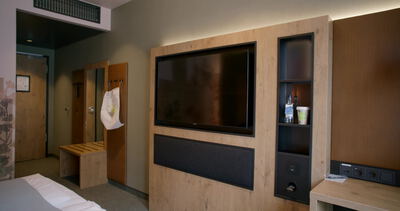 Wandmontierter Fernseher im Holzschrank steht neben Minibar Regal im Hotelzimmer