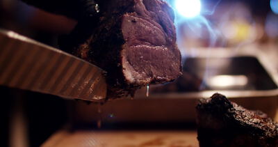 Messer schneidet dampfendes Steak im warmen Gegenlicht