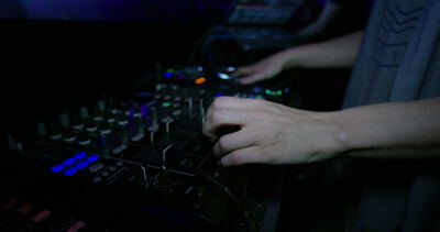 Ein DJ bedient das Mischpult mit beiden Händen im dunklen Club