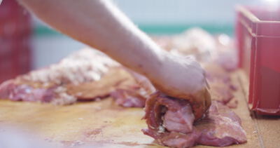 Eine Hand rollt gefüllte Rouladen auf dem Holztisch der Fleischerei