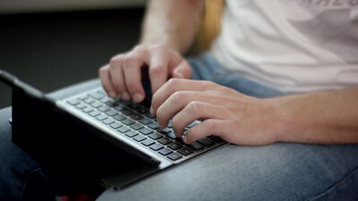 Mann tippt auf einem Laptop auf dem Schoß