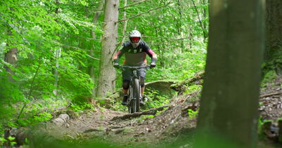 Mountainbiker fährt auf einem Waldtrail an der Kamera vorbei