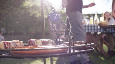 Schwenkgrill mit Steaks und Bratwürsten bei einem sonnigen Gartenfest