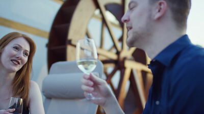 Paar stößt mit Weißwein im Freien an einem Wasserrad an