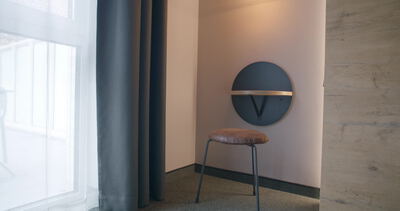 Runder Wandspiegel mit Lampe leuchtet über Designerstuhl im Hotelzimmer