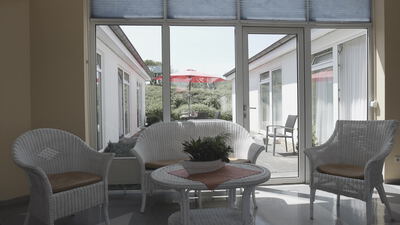 Heller Wintergarten mit weißen Rattanmöbeln und Blick auf die Terrasse