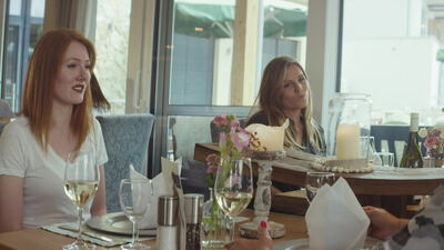 Zwei Frauen unterhalten sich bei Weißwein am Restauranttisch