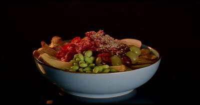 Bowl mit Brokkoli Edamame und roter Sauce beim Übergießen vor dunklem Hintergrund