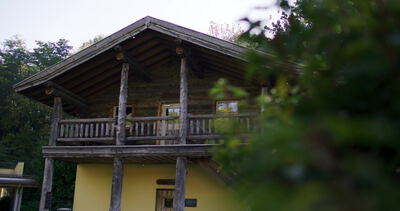 Alpines Holzhaus mit Balkon durch Blätter hindurch gefilmt
