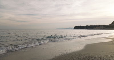 Wellen laufen bei bedecktem Himmel an einem stillen Strand aus