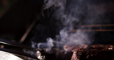 Grillzange hält gegrilltes Fleisch über hohe Flammen im Dunkeln