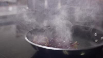 Rote Früchte werden in der Pfanne über dem Herd geschwenkt, Früchte in der Pfanne, rote Früchte kochen und Früchte schwenken