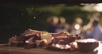 Gewürz rieselt im Abendlicht auf frisch aufgeschnittenes Steak