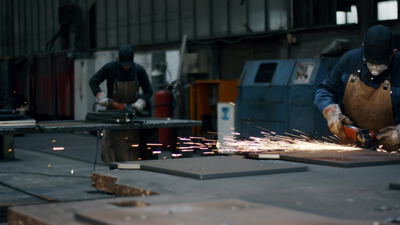 Metallarbeiter mit Lederschürze schleift Stahl in einer Fabrikhalle
