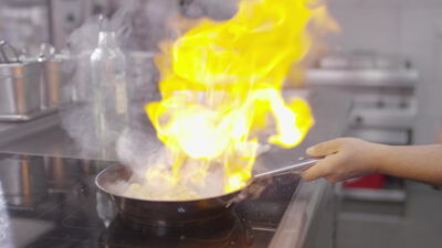 Koch flambiert ein Gericht in der Pfanne über offener Flamme