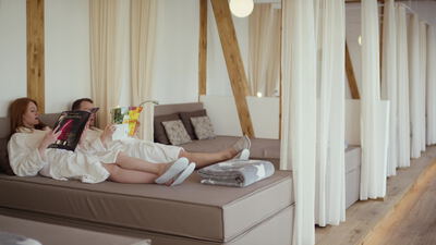 Frau im Bademantel liest Zeitschrift auf der Wellnessliege