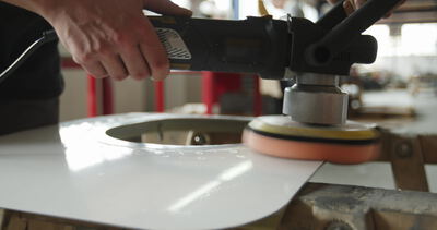 Hände polieren ein glänzendes weißes Kunststoffbauteil mit einer Poliermaschine