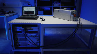 Technischer Versuchsaufbau mit Laptop und Messgeräten auf einem Labortisch bei blauem Licht