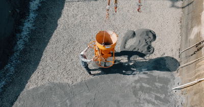 Vogelperspektive auf Bauarbeiter beim Entleeren eines Betonkübels am Kran in einer Baugrube