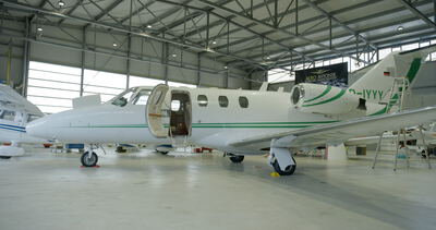 Weißer Privatjet mit grünen Akzenten und geöffneter Kabinentür in einer hellen Flugzeugwartungshalle