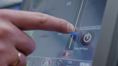 Zeigefinger bedient einen blauen Schieberegler auf einem digitalen Touchscreen Monitor