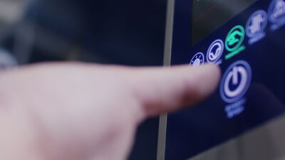 Zeigefinger drückt die beleuchtete Start und Stop Taste auf einem blauen Bedienfeld