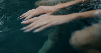 Zwei Hände gleiten sanft durch dunkles Wasser in einem Pool oder Spa